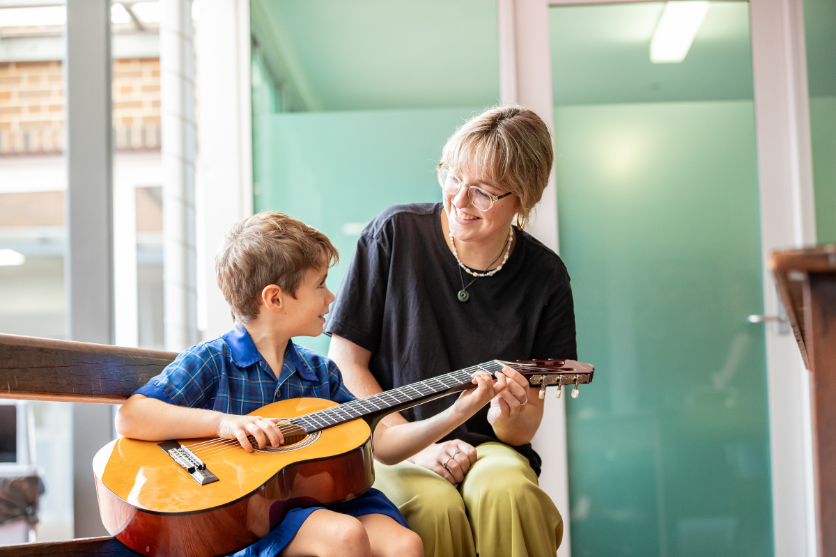 Student learning to play the guitar with teacher guidance, highlighting music education, skill development and supportive teaching at Holy Spirit School