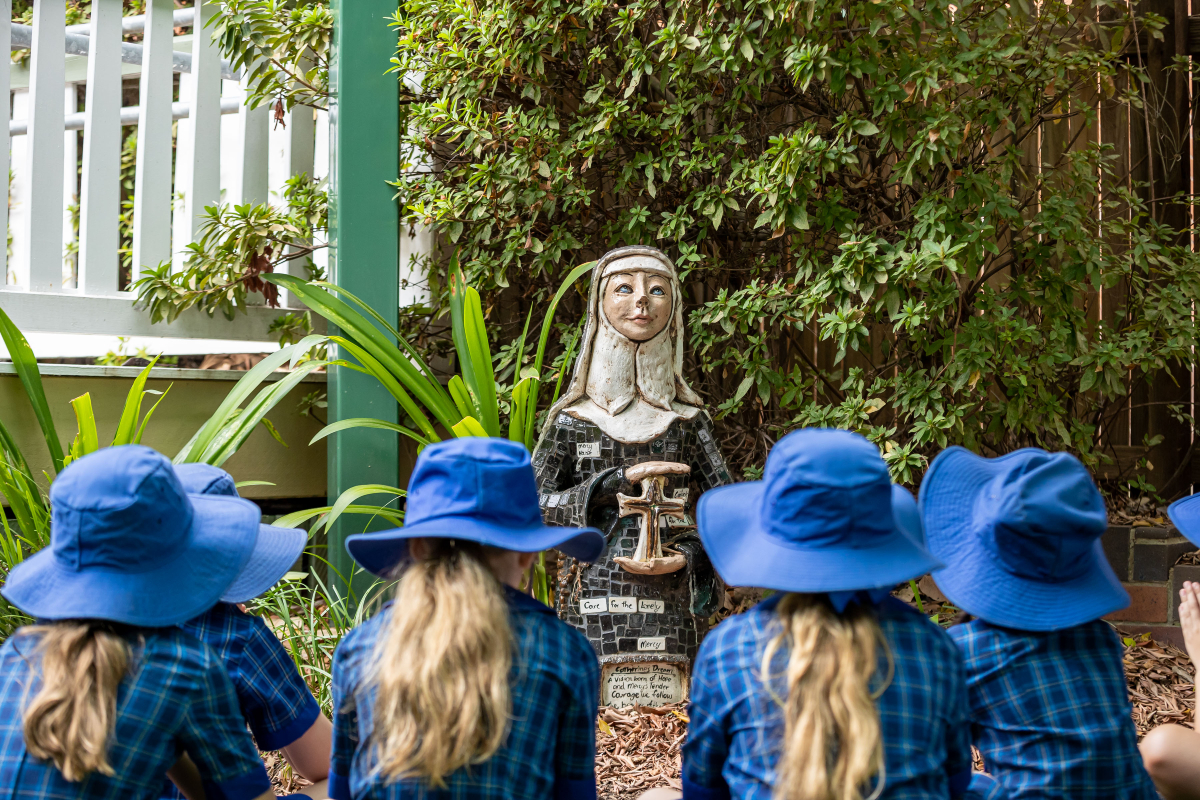Students gathered outdoors in reflection around a statue representing Catherine McAuley, highlighting Catholic identity, mercy values and shared prayer within the Holy Spirit School community